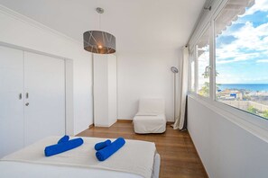 Et hotelværelse med seng, stol, stort vindue med havudsigt og en hængende lampe.