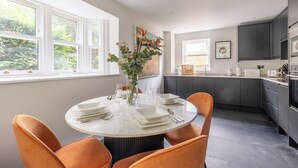 A modern kitchen with grey cabinets, a round dining table with orange chairs, and a vase with flowers. - Birdsong Cottage - North East Escapes (Belford)