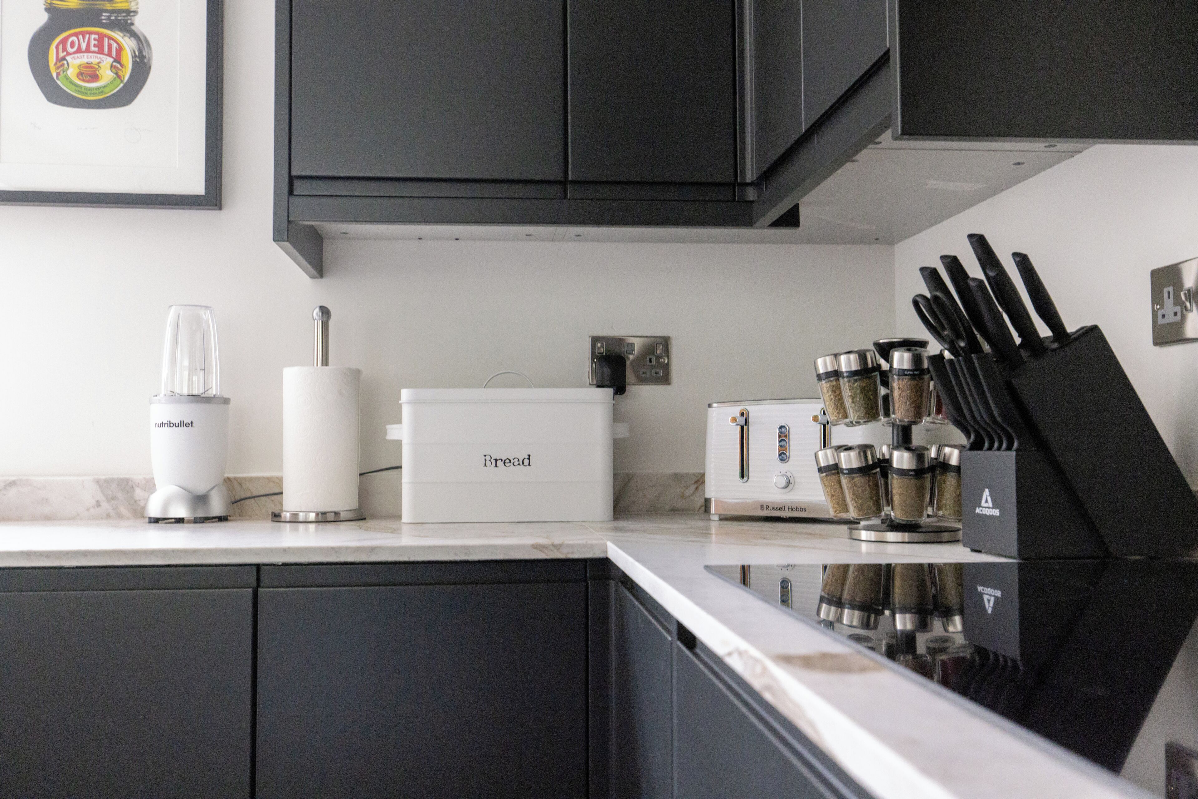 A kitchen with dark cabinets, a white countertop, a bread box, a toaster, a blender, and a knife block.