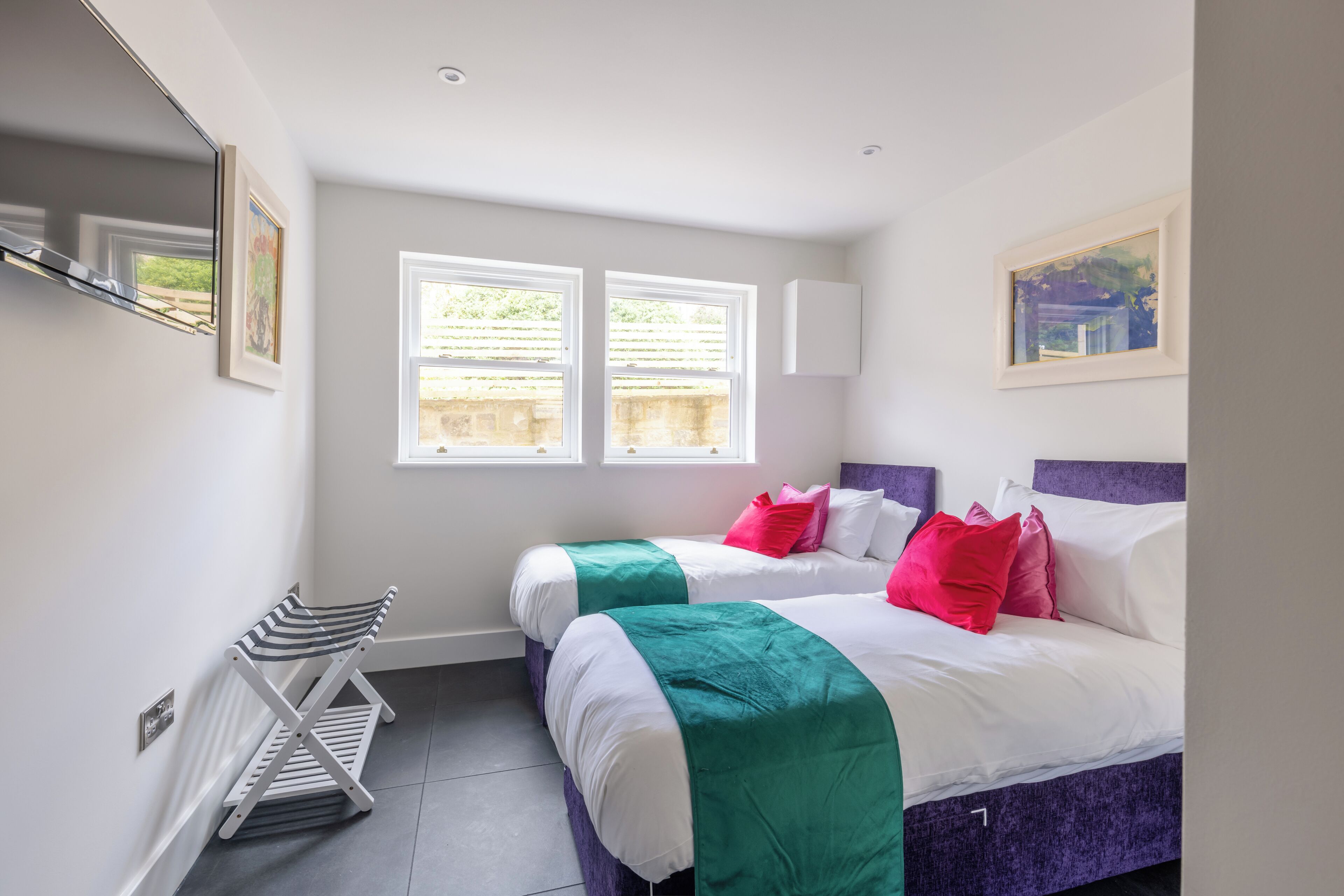 A bedroom with two beds, a bench, and two windows.