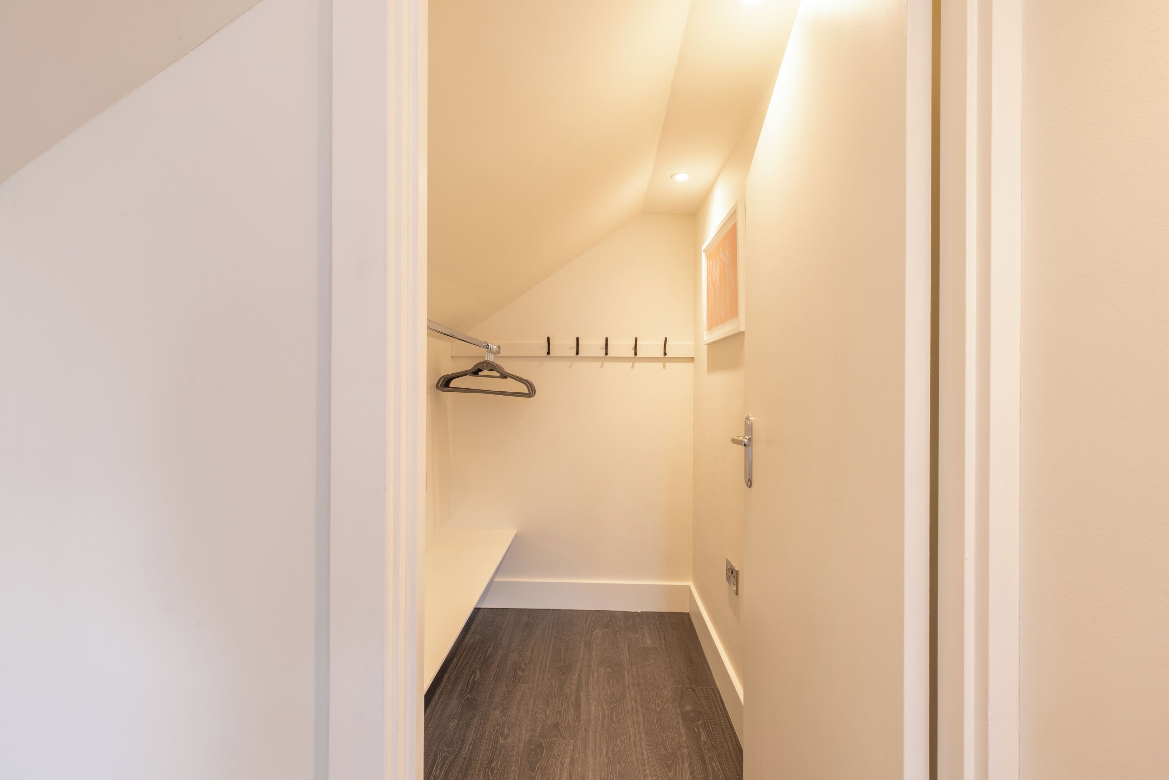 A narrow hallway with a wooden floor, a coat rack, and a door on the right.