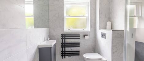 Une salle de bain moderne avec des toilettes blanches, un porte-serviettes noir et une fenêtre laissant entrer la lumière naturelle.