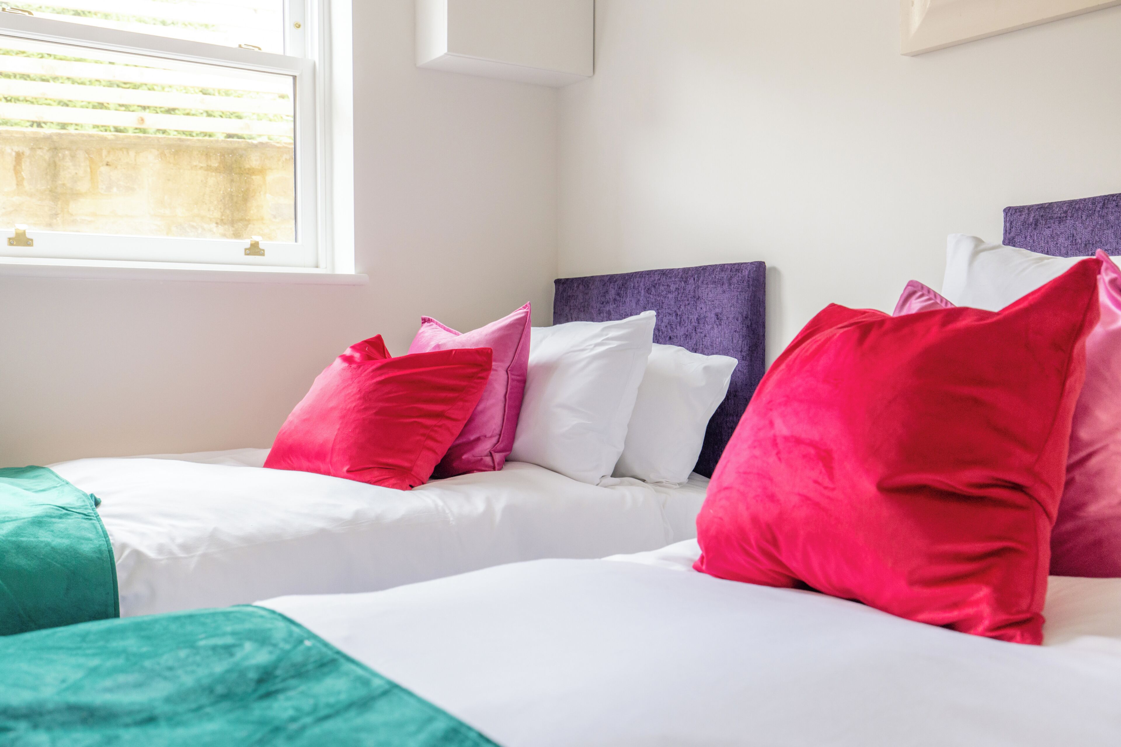 A hotel room with two beds, each with white bedding and multiple pillows in red, pink, and green.