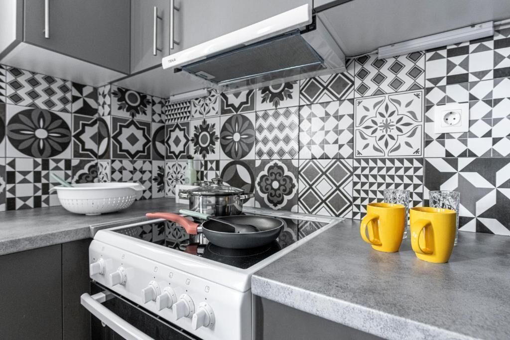 A kitchen with a gas stove, a pot on the stove, and two yellow mugs on the counter.