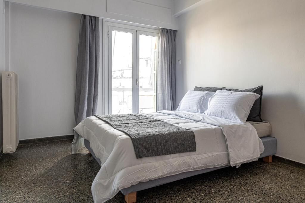 Un dormitorio con cama, cortinas grises, un radiador y una ventana.
