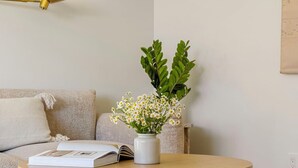 Une table ronde en bois, sur laquelle sont posés un vase blanc rempli de fleurs et un livre, le tout placé sur un tapis à motifs.