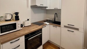 Una cucina compatta con mobili bianchi, un piano di lavoro in legno, forno a incasso, microonde, bollitore, tostapane e lavello.