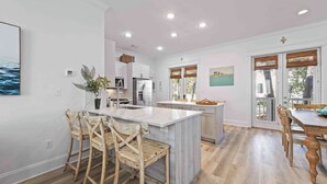 A modern kitchen with white cabinetry, a central island, and wooden chairs. - Seagrove’s 30A Window to Heaven: Pool and Beach (Santa Rosa Beach)