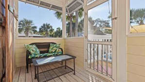 A covered porch with a wicker sofa and a small table, overlooking a residential area with palm trees. - Seagrove’s 30A Window to Heaven: Pool and Beach (Santa Rosa Beach)