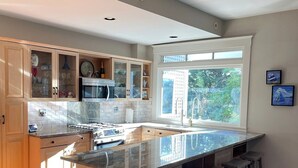 A modern kitchen with a large island, wooden cabinets, and a view of the outdoors.