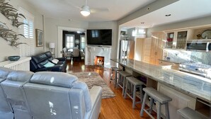 A modern living room with a grey sofa, a fireplace, and a kitchen area with a marble countertop and bar stools.