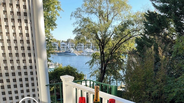 A round white table with two chairs on a wooden deck, overlooking a marina with boats and a city skyline in the background.