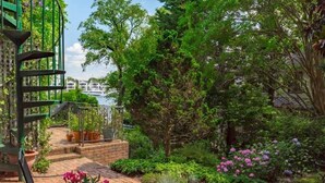 A garden with a brick pathway, potted plants, and a metal staircase leading to a balcony.