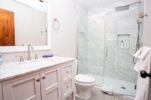Um banheiro moderno com pia de mármore, vaso sanitário e chuveiro com cabine de vidro.