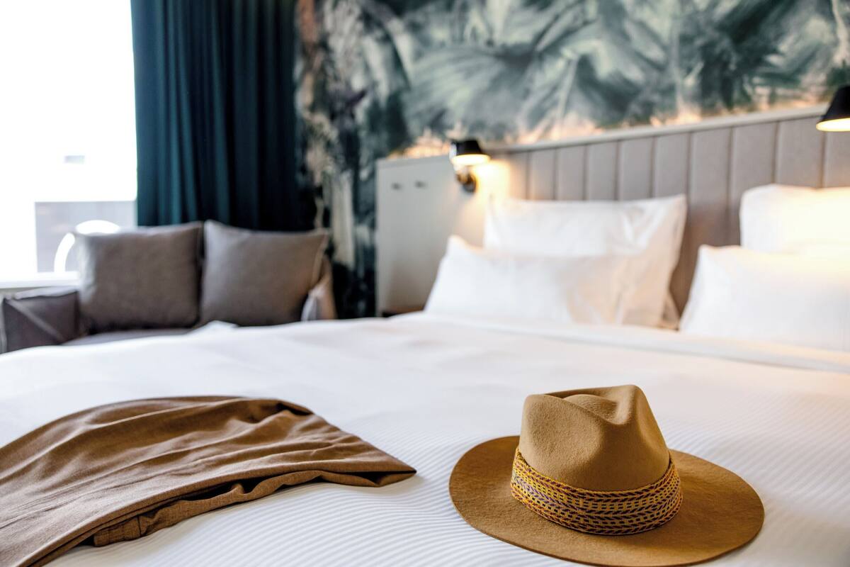A neatly made bed with a brown hat and a brown garment on it.