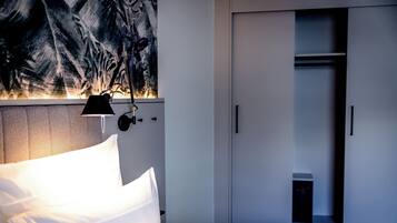 A hotel room with a bed, a nightstand, a wall-mounted lamp, and a wardrobe.