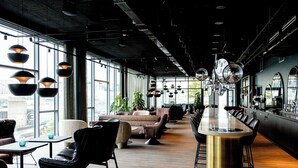 A modern interior with a long bar, leather seating, and large windows. - Motel One Paris - Porte de Versailles (Issy-les-Moulineaux)
