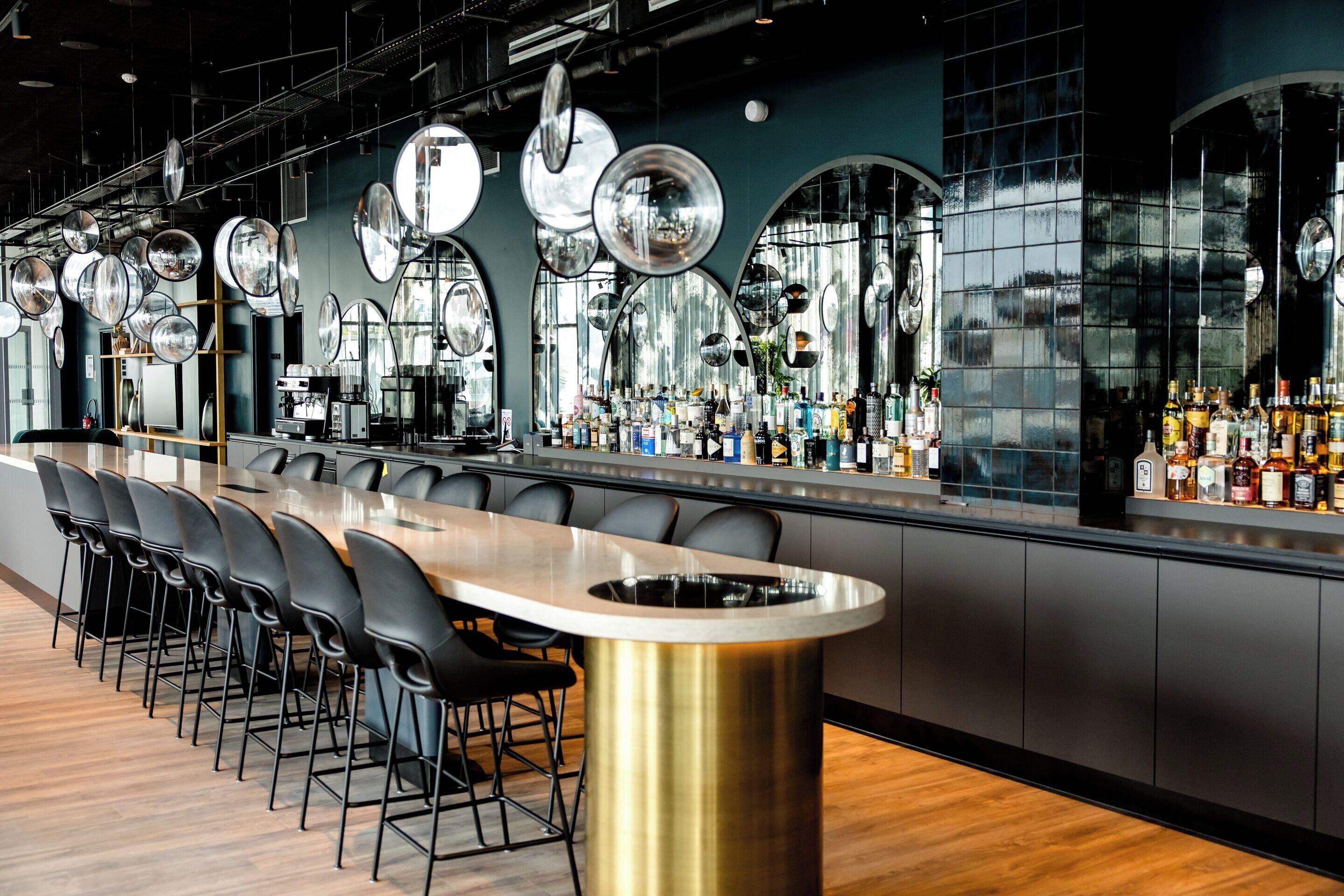 Un bar moderno con una barra larga, varios espejos y una gran variedad de botellas.