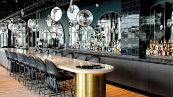 Un bar moderno con una barra larga, varios espejos y una gran variedad de botellas.