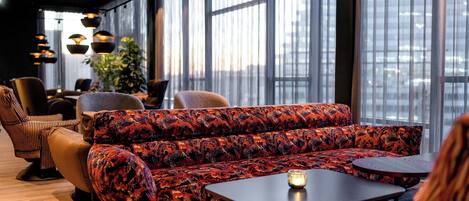 Un área de estar moderna con un sofá estampado, sillones de cuero y una mesita con una vela.