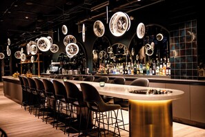 Un'area bar moderna con un lungo bancone, sedie nere e lampade a sospensione circolari.