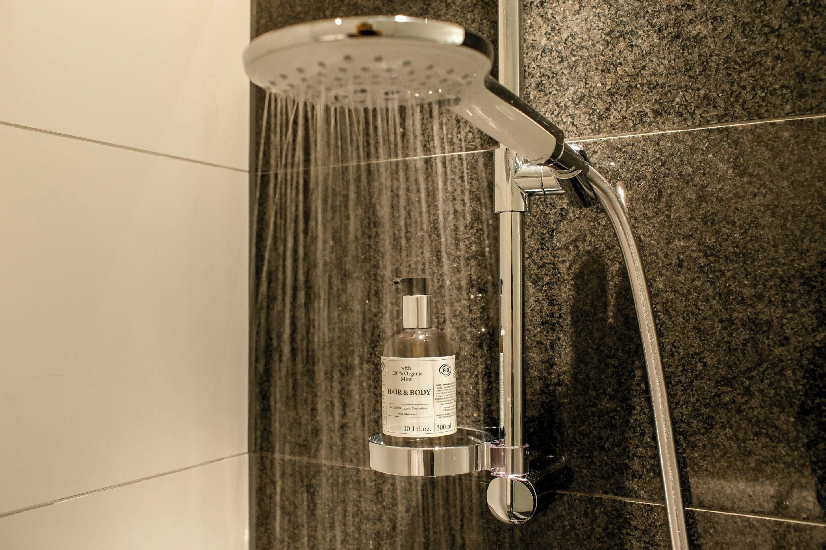 Una ducha con un cabezal de ducha de mano y una botella de jabón para cabello y cuerpo.