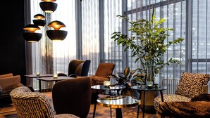 A modern lounge area with leather chairs, a glass coffee table, and a large window with sheer curtains. - Motel One Paris - Porte de Versailles (Issy-les-Moulineaux)