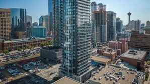A high-rise building with a modern glass facade, surrounded by other tall buildings and a parking lot. - Tower Views! Pool, FREE Banff Pass! (Calgary)