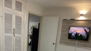 Quarto de hotel com uma cama, televisão fixada na parede e porta de acesso a outro espaço.