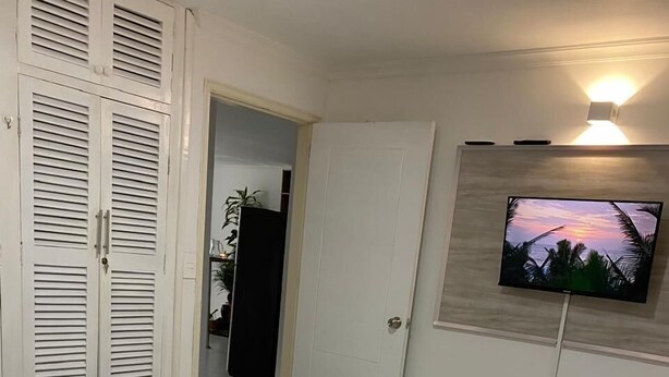 Ein Hotelzimmer mit einem Bett, einem an der Wand befestigten Fernseher und einer Tür zu einem weiteren Raum.
