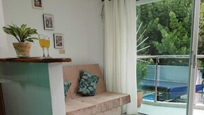 Ein modernes Wohnzimmer mit einer Couch, einem Glastisch und einem Essbereich mit Tisch und Stühlen. Ein Schiebeglasfenster führt auf einen Balkon mit Pool.