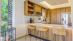 Une cuisine moderne avec des meubles en bois, un réfrigérateur en acier inoxydable et un coin bar doté de tabourets en osier.