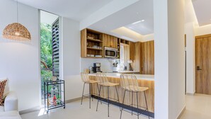 Une cuisine moderne avec des meubles en bois, un four à micro-ondes encastré et un coin bar agrémenté de trois chaises en osier.