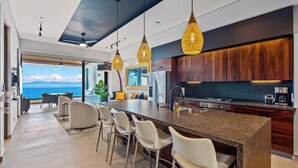 A modern kitchen with a large island, stainless steel appliances, and a view of the sea.