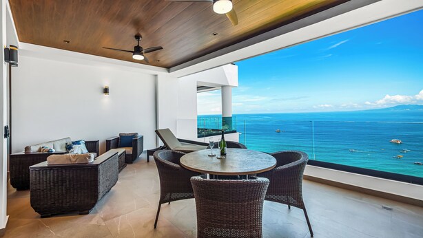 A balcony with wicker furniture, a table with a bottle and glass, and a view of the ocean.
