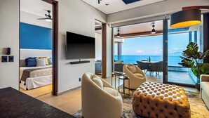 A modern hotel room with a bed, seating area, and a balcony with a view of the ocean.