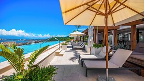 An infinity pool with a view of the city skyline, lounge chairs, and umbrellas.