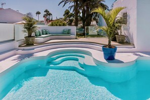 Una piscina con borde curvo, rodeada de muros blancos y plantas verdes.
