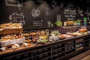 A bakery counter with various baked goods and a chalkboard wall with greetings and product names. - Motel One München-Hauptbahnhof (Munich)