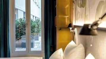 A hotel room with a large window, a view of the outside, a bed with white bedding, and a wall-mounted lamp.