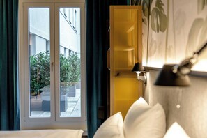 A hotel room with a large window, a view of the outside, a bed with white bedding, and a wall-mounted lamp. - Motel One München-Hauptbahnhof (Munich)