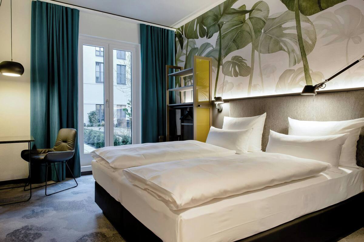 A hotel room with a large bed, a chair, a desk, and a view of the outside.
