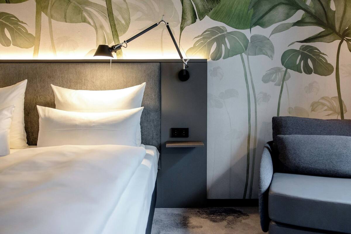Quarto de hotel com cama, abajur, mesa de cabeceira e uma cadeira.