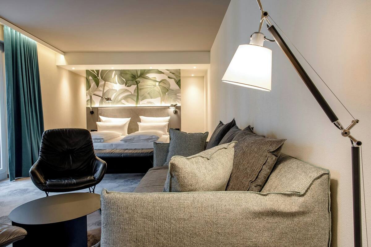 Quarto de hotel moderno com cama, sofá, poltrona e luminária.