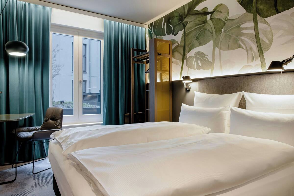 Quarto de hotel com cama, escrivaninha, cadeira e vista para o exterior.