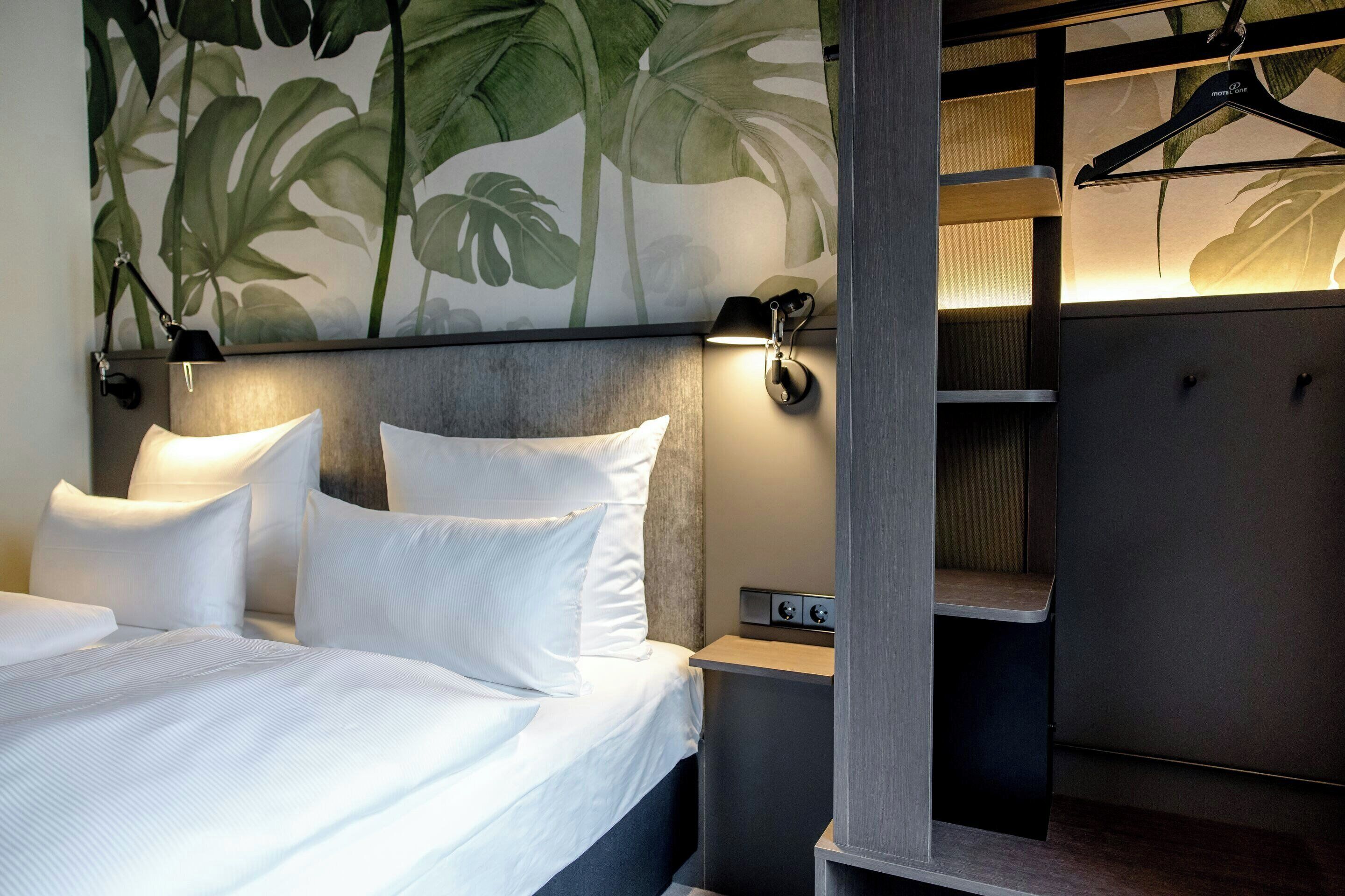 Una habitación de hotel moderna con una cama grande, dos lámparas de noche, una mesita de noche y un armario con perchero.
