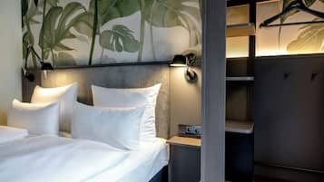 Una habitación de hotel moderna con una cama grande, dos lámparas de noche, una mesita de noche y un armario con perchero.