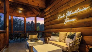 A cozy wooden cabin interior with a stone coffee table, wicker sofa, and a neon sign reading "Fresh Mountain Breeze". - Shenandoah Mansion (Elkton)