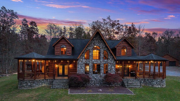 A log cabin with a stone foundation, multiple chimneys, and a porch with string lights. - Shenandoah Mansion (Elkton)