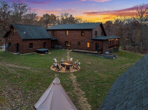 A log cabin with a fire pit and outdoor seating, surrounded by a grassy yard and trees. - Shenandoah Mansion (Elkton)